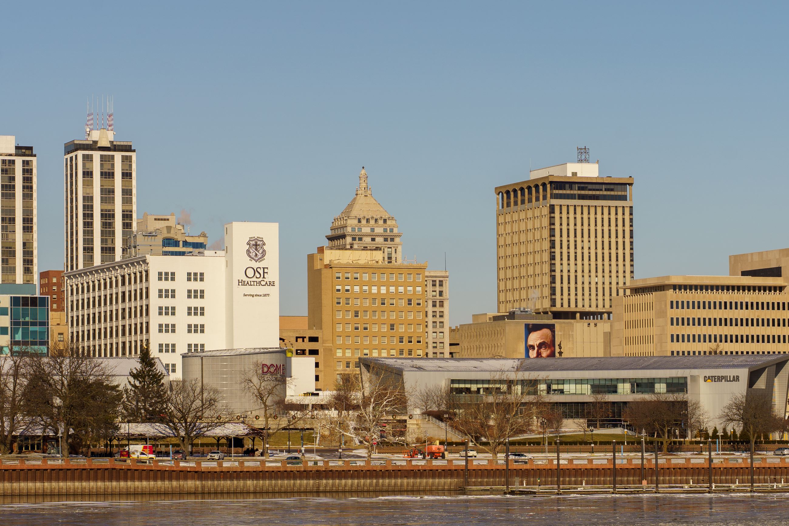 Photo of a city skyline along a riverfront, featuring a mural of Abraham Lincoln's face.