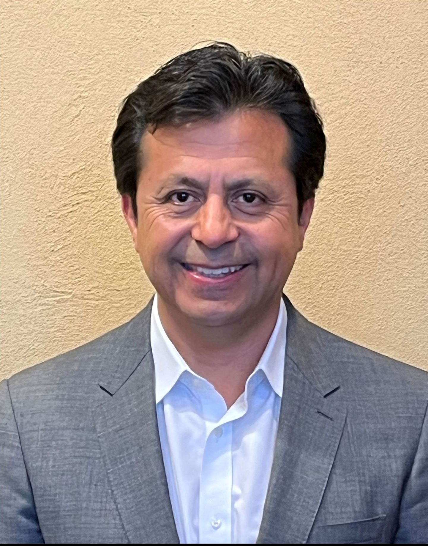 Headshot of a man wearing a shirt and a jacket smiling.